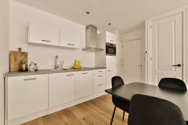 Beyaz dolapları, siyah sandalyeleri ve tezgahın üstünde fırını olan bir evde mutfak ve yemek odası.