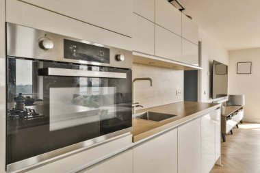 Beyaz dolapları ve ahşap tezgahları olan modern bir mutfak ve arka plandaki duvarda bir fırın.