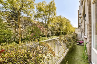 Evin her iki tarafında çiçek açan saksılarda bitki ve ağaçların olduğu arka bahçenin manzarası.