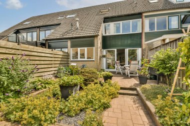 Önünde bitkiler olan bir ev ve diğer tarafında da bahçe bahçesi olan ahşap bir çit var.