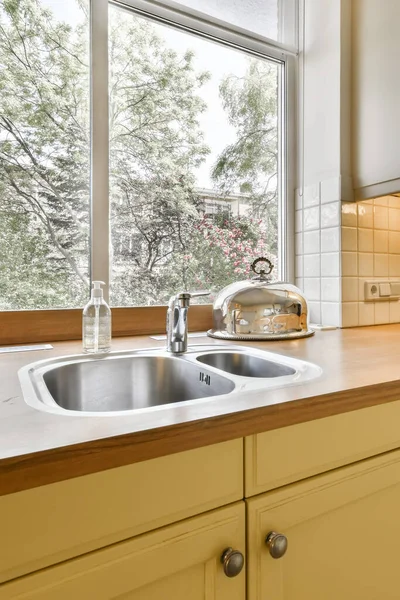 a kitchen with a sink and window in the back ground looking out to the trees outside through the glass door