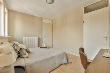 Odanın önündeki duvarda yatağı, masası ve aynası olan bir yatak odası açık kahverengidir.