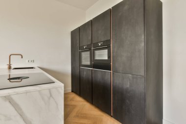 Duvarında siyah dolaplar ve beyaz mermer tezgahları olan modern bir mutfak bakır musluklu bir lavabo.