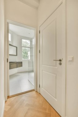 Beyaz duvarları ve ahşap döşemeleri olan boş bir oda arka planda bir mutfağı ortaya çıkarmak için açık.