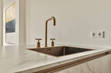 Mermer tezgahlı beyaz bir mutfak ve fotoğraftaki bakır fae lavabosu yukarıdan çekiliyor.