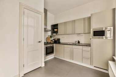 Beyaz dolapları ve siyah tezgahları olan bir mutfak. Başka bir odaya açılan açık bir kapının önünde.