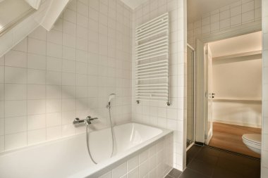 Duvarlarında beyaz fayanslar olan bir banyo ve küvetin yanında açık bir duş kabini.