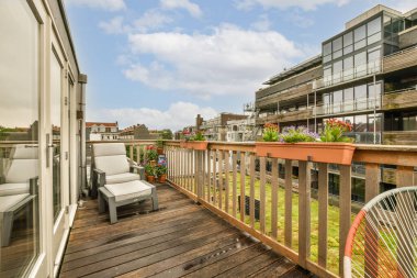 Bir apartmanın önündeki güvertede sandalye ve bitkilerle dolu bir balkon. Dışarıdan çekilmiş.