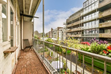 Korkulukların üzerinde çiçekler ve bitkiler olan bir balkon beyaza boyanmış bir apartmanın önünde.