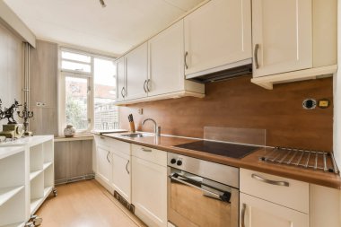 Bulaşık makinesinin önündeki tezgahlarda beyaz dolapları ve ahşap tezgahları olan bir mutfak görülebilir.