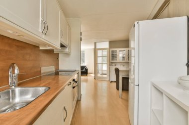 Lavabonun önünde beyaz dolapları ve ahşap tezgahları olan bir mutfak açık bir kapıdır.