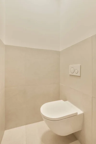 a toilet in the corner of a room with beige tiles on the walls, and a wall mounted light above it