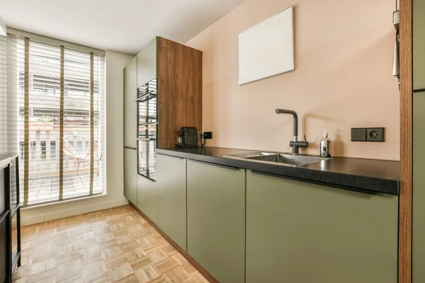 a kitchen area with wood flooring and green cabinets in the room is an open window that looks out onto the street