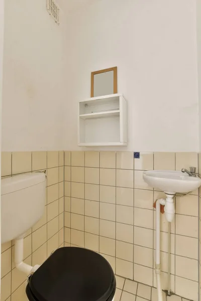 a bathroom with black and white tiles on the walls, toilet bowl is in the center of the room next to the sink