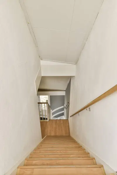 some stairs going up the side of a building with white walls and wooden steps leading to an open area in the room