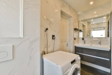 Köşesinde çamaşır makinesi ve kurutma makinesi olan bir çamaşır odası. Duvarlarında beyaz mermer var.