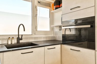 Modern bir mutfak, siyah tezgahlı ve arkasında beyaz dolaplar var. Dışarıya bakan bir pencere.