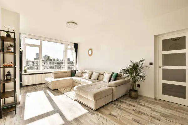 a living room with white walls and wood flooring in the middle of the room, there is a large window looking out onto the city skyline