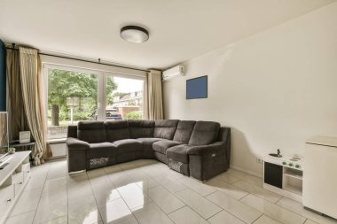 Oturma odası. Kanepesi, televizyonu ve penceresi var. Evin önündeki sokağa bakıyor.