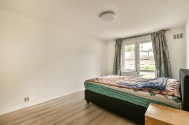 Ahşap döşemeli bir yatak odası ve pencerenin önünde dışarıdaki sokağa bakan bir yatak odası.