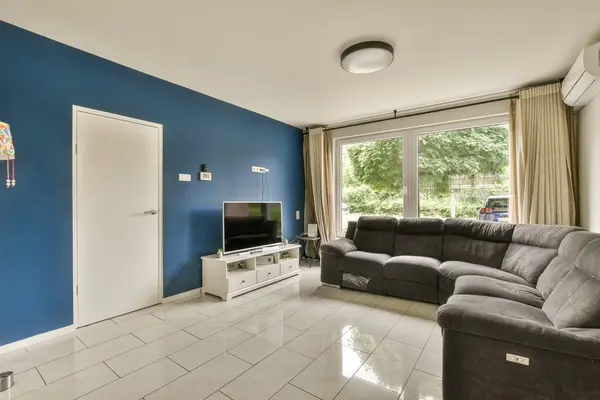 a living room with blue walls and white tiles on the floor, there is a grey couch in front of it