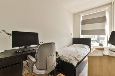 Pencerenin önündeki duvarda yatak odası, masa ve bilgisayar monitörü var.