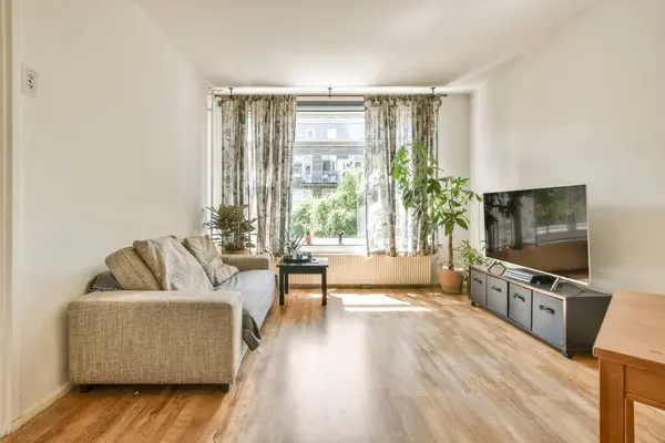 Ahşap döşemeleri ve beyaz duvarları olan bir oturma odası. Sokağa bakan büyük bir pencere de dahil.