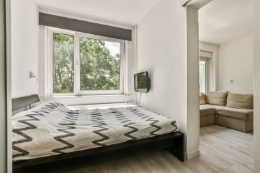 a bedroom with white walls and wood flooring the room has a large window that looks out onto the trees outside