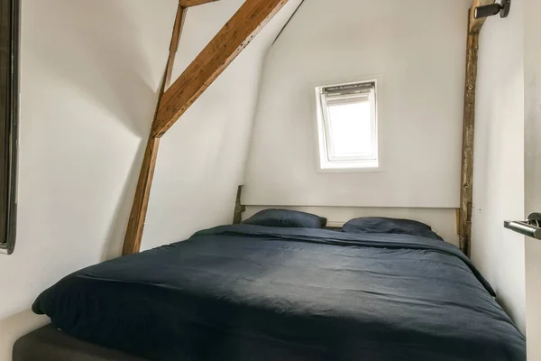 a bed in the corner of a room with an attic style window and wooden beams on the wall above it