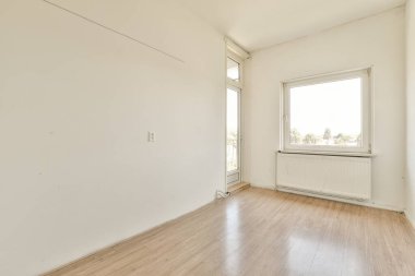 Ahşap döşemesi ve duvarlarında beyaz boya olan boş bir oda. Köşesinde bir pencere var.