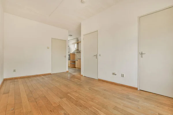an empty living room with wood flooring and white walls on either side of the room, there is a kitchen in the corner