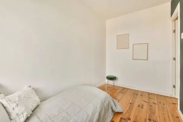 a bedroom with wood flooring and white walls, including a bed in the fore - image taken from above