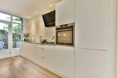 Ahşap döşemeli bir mutfak ve görüntünün ortasında beyaz dolaplar bir verandaya açılan açık bir kapı.