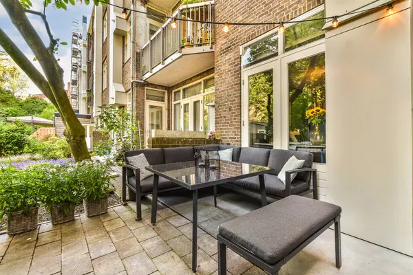 a patio with two chairs and a table in front of an apartment building that has plants growing on the outside wall