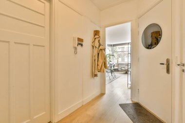 Beyaz duvarları ve ahşap döşemeleri olan bir koridor, oturma odasına açılan bir girişi gözler önüne sermek için açık.