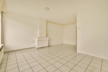 Beyaz duvarları ve yerde döşemeleri olan boş bir oda, içinde kimse yok.