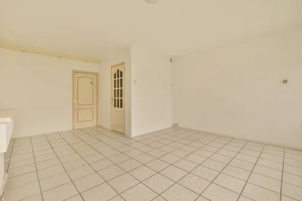 an empty room with white walls and floor tiles on the floor, there is a door in the corner that leads to another room
