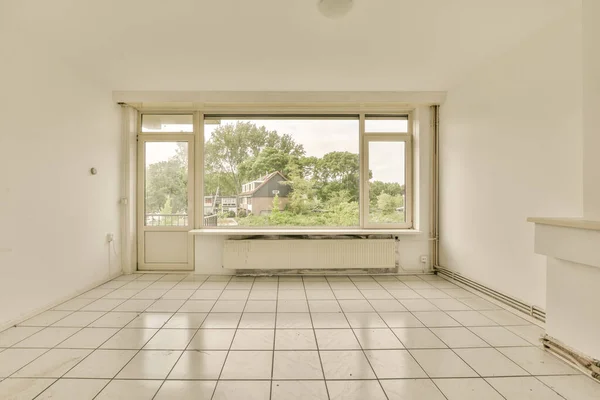 an empty room with white tile flooring and large windows looking out onto the trees in the distance are buildings