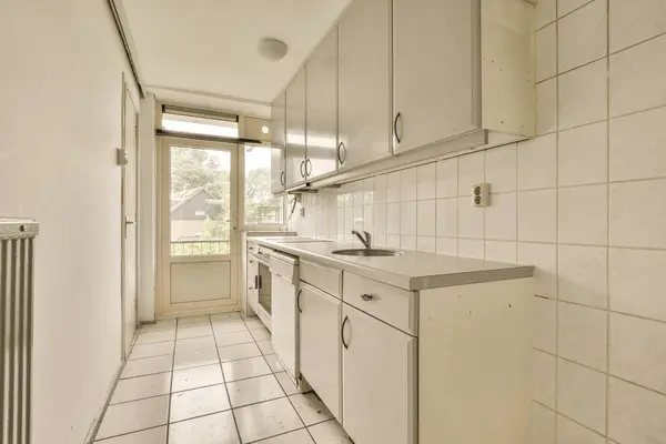 a kitchen with white tiles on the floor and cabinets in the corner, looking towards the entrance to the back door