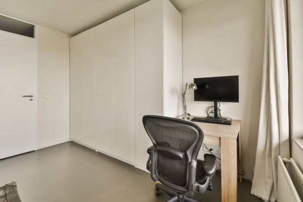 a room with an office chair, desk and television monitor on the wall in the room is very white color