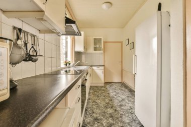 Bu fotoğraftaki tezgahların üzerinde beyaz dolaplar ve siyah tezgahlar olan bir mutfak alanı içeriden çekilmiş.