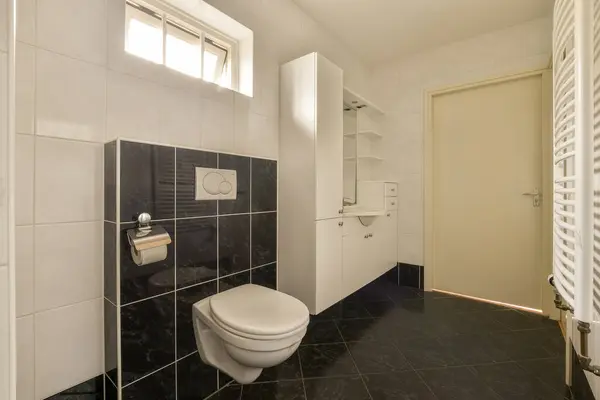 a bathroom with black and white tiles on the walls, toilet paper rolls in front of the door to the room
