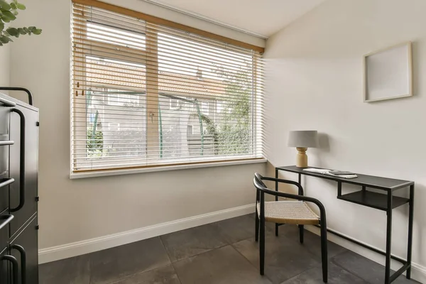 an empty room with wooden blinds and a small desk in front of the window there is a plant on the table