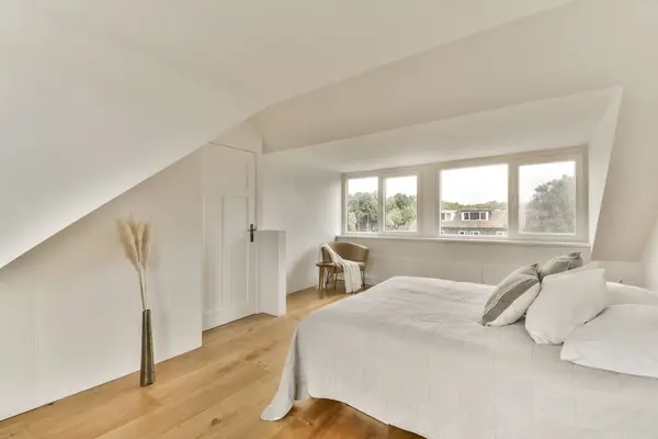 a bedroom with white walls and hardwood flooring in the room, there is an empty bed on the right side