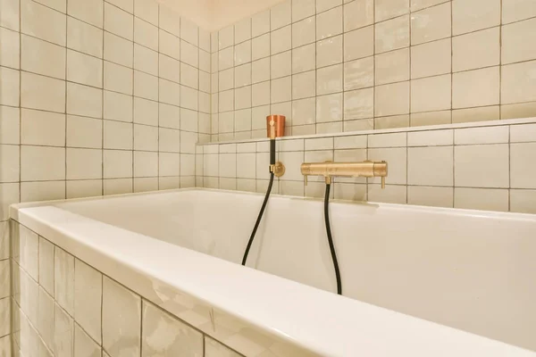 a bathtub in a bathroom with white tiles on the walls, and a black shower hose attached to the tub