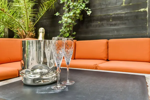 two wine glasses on a table with an orange couch in the photo is taken to the right, and its not clear