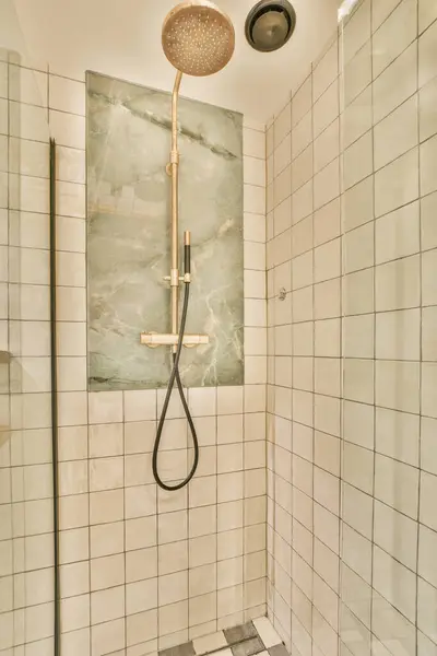 a shower in a bathroom with white tiles on the walls, and a black shower head mounted to the wall