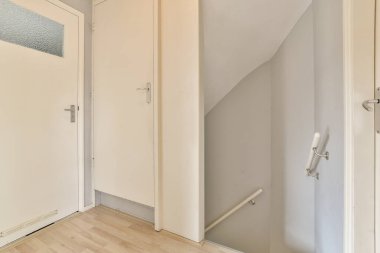 Beyaz duvarları ve sağ tarafında ahşap döşemeleri olan boş bir oda. Sol köşede kapalı bir kapı var.