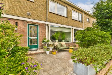 Önünde çiçekler ve bitkiler olan bir dış alan. Pencereli bir köşe. Beyaza boyanmış tuğla bir duvarın yanında.