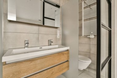 Duvarlarında ahşap dolaplar, beyaz fayanslar ve odanın ortasında bir tuvalet olan modern bir banyo.